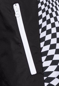 Czarna tkanina z białym zamkiem błyskawicznym i sekcją z czarno-białym wzorem w kratkę, prezentująca gładką teksturę i kontrastujące wzory.