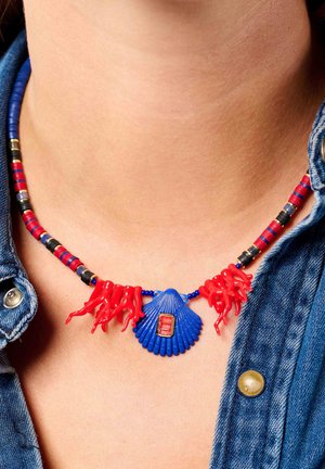Buntes Halsband mit roten korallenartigen Akzenten, einem blauen muschelförmigen Anhänger und mehrfarbigen Perlensträngen, vor einem Jeanshintergrund.