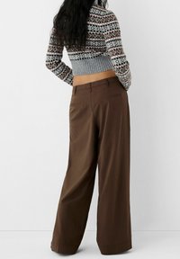 Bruna byxor med vida ben och en slät yta, med bakfickor och medelhög midja, i kombination med en mönstrad kort tröja.