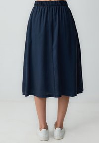 Marineblaue Midi-Rock mit einem elastischen Bund, glatter Textur und ausgestelltem Schnitt, kombiniert mit weißen Sneakers vor einem neutralen Hintergrund.