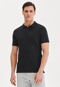 Czarna koszulka polo z miękkiego materiału, taliowana, z trzema guzikami oraz subtelnym logo marki na piersi. Krótkie rękawy i płaski kołnierzyk.