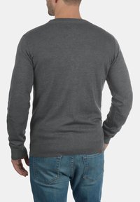 Grå strikkegenser med rund hals, ribbestrikkede mansjetter og nederkant, samt albueflekker, kombinert med blå denimjeans. Vist fra baksiden.