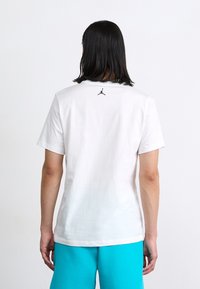 Hvid bomulds t-shirt med korte ærmer, prydet med et sort Jumpman-logo på den øverste ryg. Glat tekstur og klassisk crew neck-design.