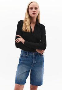 Schwarzes Langarm-Polohemd mit einem Notch-Kragen, kombiniert mit hellblauen Jeansshorts, die einen fransigen Saum und einen lockeren Schnitt aufweisen.