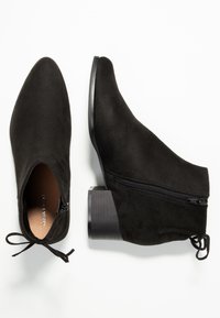 Czarne zamszowe botki za kostkę z ostrym noskiem, bocznym zameczkiem i niskim słupkowym obcasem. Charakteryzują się eleganckim wyglądem i gładką teksturą.