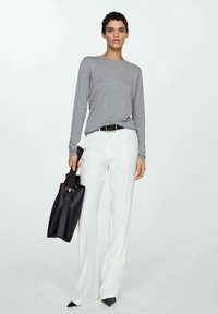 Sivi dugi rukav, bijele široke hlače i crna torba. Outfit ima strukiranu siluetu s remenom, elegantne linije i crne štikle s oštrim vrhom.