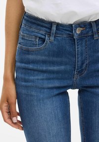 Jean en denim bleu foncé avec un design ajusté, taille haute et style classique à cinq poches. Présente des coutures visibles et une fermeture à bouton en métal.