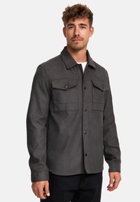 Camisa de botones de color gris oscuro con cuello, que presenta dos bolsillos en el pecho y una textura suave; diseñada para un aspecto casual.