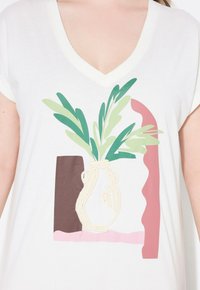 Hvid bomulds t-shirt med v-hals, der har et grafisk motiv af en vase med grønne blade og abstrakte former i brun og pink.