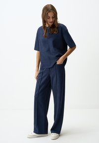 Navyblauw tweedelig outfit gemaakt van zachte, soepele stof. T-shirt met korte mouwen en een ruime pasvorm, gecombineerd met bijpassende wijde broek. Witte sneakers.