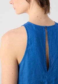 Blå linneärmlös topp med en nyckelhålsöppning bak och knappstängning. Slät textur och enkel design.