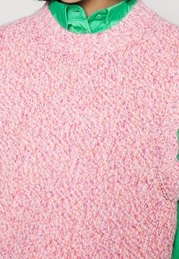 Lähikuvassa on roosa ja oranž kudottu neulepusero kirkkaan vihreän kauluspaitakauluksen päällä.