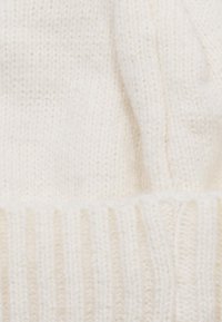 Cappello a maglia crema con un design a coste e una texture morbida. Caratterizzato da un bordo aderente nella parte inferiore, adatto per calore e comfort.