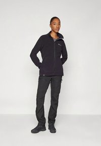 Svart fleecejakke med høy krage og glidelåslukking, kombinert med svarte cargobukser og tursko, som skaper et koordinert utendørsantrekk.