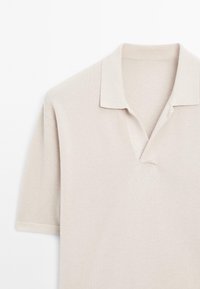Polo beige à manches courtes avec un tissu texturé et un col doux, présenté sur fond blanc.