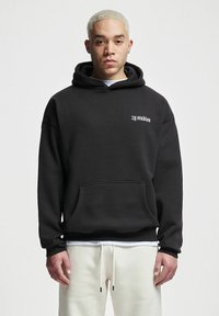 Musternööriga must kapuutsiga dressipluus, mis on valmistatud puuvilla segust, esiküljel on tasku ja vasakul rinnal väike valge logo. Fliisist sisetunne.