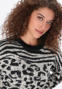 Zwart-wit trui met een fuzzy textuur en zebra- en luipaardpatronen, versierd met pailletten en een zwarte ribbelkraag.