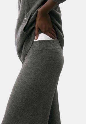 Grau gestrickter Pullover mit einer weichen Textur, der eine lockere Passform und seitliche Taschen aufweist. Kombiniert mit passenden grauen Strickhosen, ebenfalls weich und entspannt.