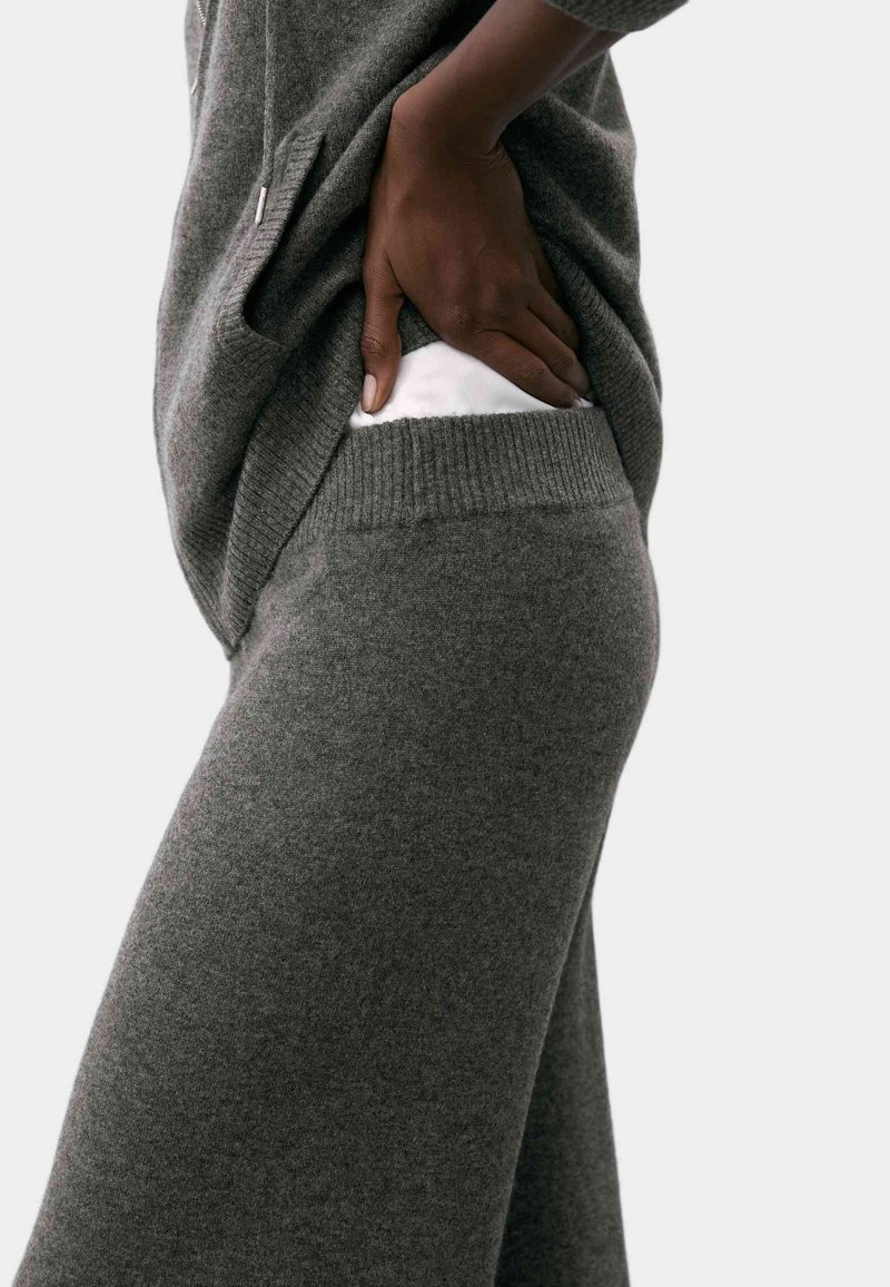 Maglione grigio a maglia con una consistenza morbida, caratterizzato da una vestibilità ampia e tasche laterali. Abbinato a pantaloni coordinati in maglia grigia, anch'essi morbidi e rilassati.