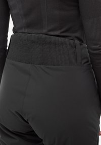 Schwarze isolierte Hosen verfügen über einen strukturierten elastischen Bund und glattes Material. Das Design ist tailliert, mit sichtbaren Nähten und einer eleganten Silhouette.