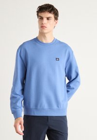 Blue cotton sweatshirt featuring a crew neckline, long sleeves, and a small navy logo on the left chest. Smooth texture and relaxed fit.