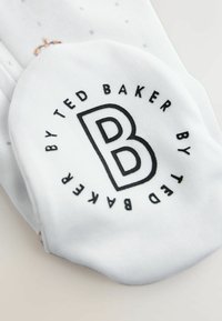 Vit strumpa med en svart cirkulär logotyp med texten "TED BAKER" och en stor "B." Mönstrad bakgrund med små grå bokstäver och en krona som detaljer.