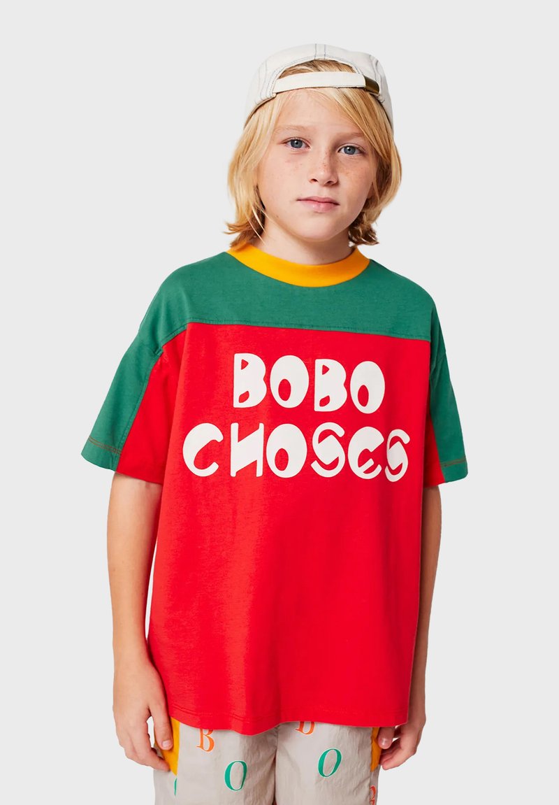 Rød og grøn kortærmet t-shirt med en gul krave og fed hvid tekst "BOBO CHOSES." Blødt stof med en afslappet pasform.