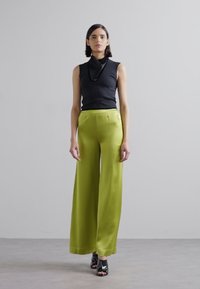 Zwarte mouwloze top gecombineerd met hooggevoerde, losse, glanzende limoen groene broek en zwarte sandalen met straps. In totaal een minimalistisch ontwerp.