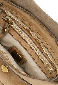 Interno di una borsa in pelle color cuoio con cerniere dorate, molteplici tasche e rivestimento in tessuto morbido. Presenta un'etichetta del marchio e una texture liscia.