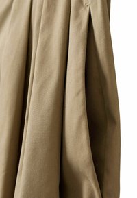 Gros plan d'un tissu beige avec des plis et des coutures visibles, montrant la texture et la chute du matériau.