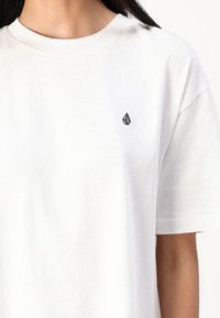 Weißes Baumwoll-T-Shirt mit Rundhalsausschnitt und kurzen Ärmeln, versehen mit einem kleinen schwarzen Logo auf der linken Brustseite. Weicher Stoff, lockere Passform.
