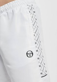 Hvite idrettsshorts laget av teksturert stoff, med en svart logo og geometrisk trykk langs siden for ekstra detaljer.