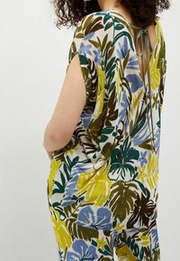 Mono de manga corta con un estampado floral que presenta hojas amarillas, azules y verdes. Espalda descubierta con cierre de lazo, tejido suave y texturizado.