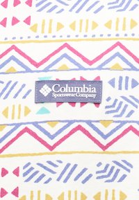 Ετικέτα Columbia Sportswear σε ύφασμα με πολύχρωμα γεωμετρικά σχέδια σε ροζ, κίτρινο, μπλε και τιρκουάζ σε λευκό φόντο.