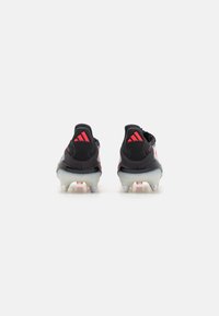 Black soccer cleats with red accents, a textured upper, and a transparent outsole. Features three red stripes on the heel.