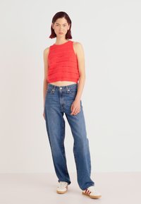 Punane ilma varrukat crop top, millel on tekstureeritud muster, koos laia lõikega siniste denim-pükste ja valgete tossudega, millel on punased ja tumesinised triibud.