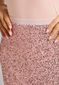 Lichtroze paillettenrok met een soepele tailleband, dicht op elkaar geplaatste glanzende pailletten en een gestructureerd oppervlak dat licht weerkaatst.