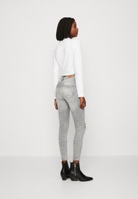 Top blanco de mangas largas, jeans ajustados de tiro alto en un gris claro con detalles desgastados, y botas negras hasta el tobillo con tacones gruesos.
