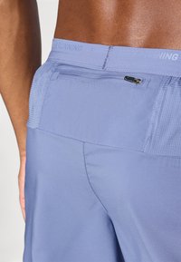 Vaaleansiniset juoksushortsit, joissa on verkkovuorinen vyötärö, vetoketjullinen tasku takana sekä sileä, kevyt kangas, jossa on hienovaraisia tekstuurityksityiskohtia.