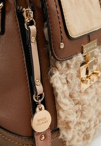 Brown handbag with a textured, fluffy beige accent, featuring gold hardware, a secure clasp, and a hangtag marked "RIVER ISLAND."
