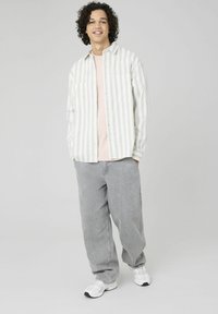 Chemise à rayures claires à manches longues en blanc et gris, portée sur un t-shirt rose. Un pantalon gris ample et des baskets blanches complètent la tenue.