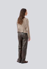 Jachetă bej scurtă cu un detaliu pliat la spate, asociată cu pantaloni largi din piele maro. Textură netedă, design minimal.
