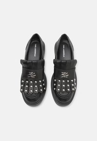 Fekete bőr slip-on cipők fém tüskékkel, redőzött pánt részlettel és a logó dombornyomattal a talpon. Kerek orrú kialakítás.