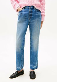 Pantalones vaqueros de denim azul con corte recto, que presentan una cintura alta, dos bolsillos frontales y un acabado desgastado. Mocasines negros como calzado.
