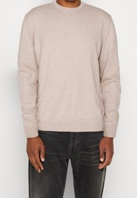 Jasno beżowy sweter z dzianiny, z okrągłym dekoltem i długimi rękawami, charakteryzujący się miękką teksturą. Zestawiony z ciemnymi dżinsami dla kontrastu.