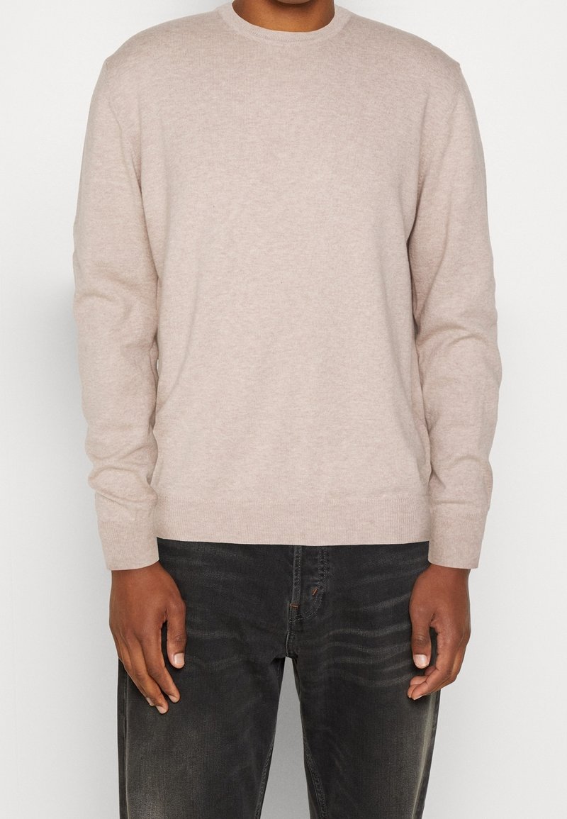 Jasno beżowy sweter z dzianiny, z okrągłym dekoltem i długimi rękawami, charakteryzujący się miękką teksturą. Zestawiony z ciemnymi dżinsami dla kontrastu.