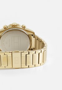 Goldfarbenes Metall-Chronographenarmbanduhr mit einem glatten Gliederarmband, rundem Gehäuse, drei Druckknöpfen und graviertem Logo der Marke auf der Rückseite.