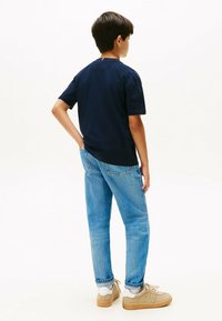 Camiseta de manga corta en azul marino con cuello redondo, combinada con jeans de mezclilla azul claro y zapatillas beiges con acentos blancos.