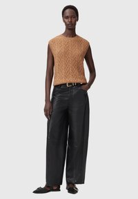 Brun strikket ærmeløs top med et tekstureret mønster, parret med brede sorte læderbukser og sorte flade sko med guldaccent.