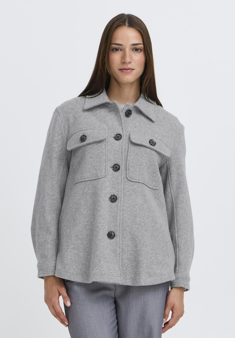 Šedá košeľa-jacket z vlnenej zmesi s golierom, dvoma náprsními vreckami a čiernymi gombíkmi. Má dlhé rukávy a voľný strih.